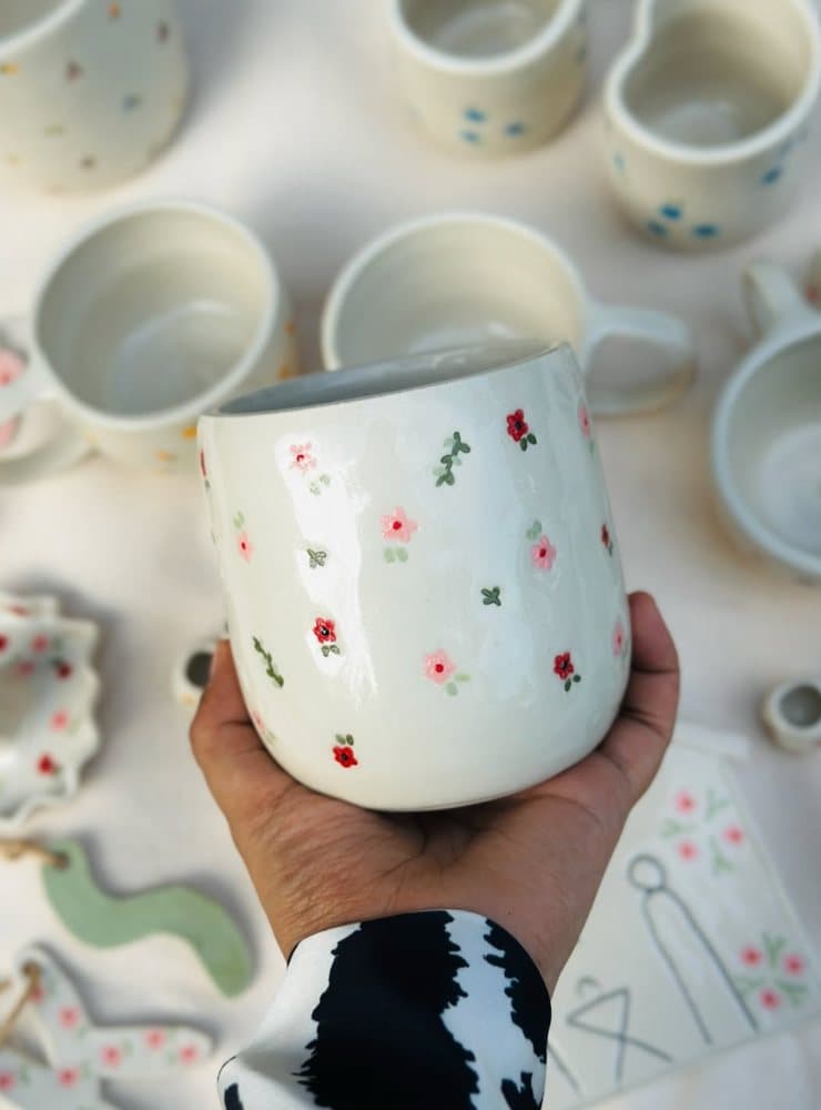 Hand holding a white ceramic mug painted with delicate floral blossoms